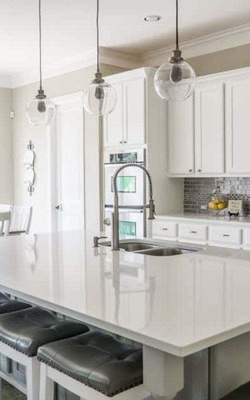 Contemporary white kitchen with island, pendant lights, and large windows.